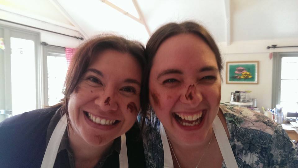 Two ladies smiling and laughing with chocolate smeared on their faces.  Having fun on a chocolate workshop experience.