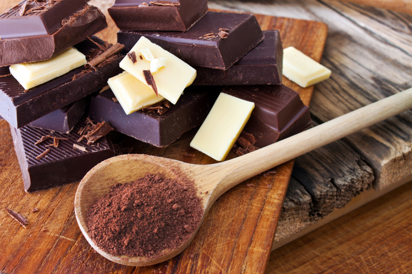 chunks of white and dark chocolate on a board with a wooden spoon filled with grated chocolate