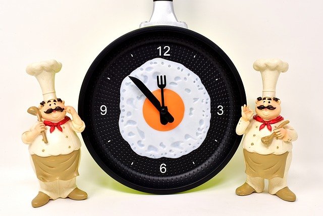 Two cartoon chefs beside a clock with an fried egg in the centre