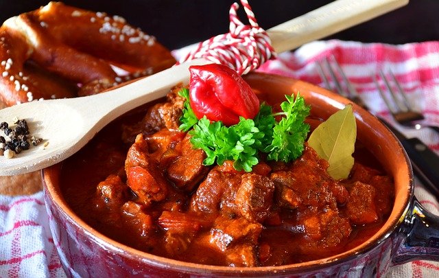 Beef goulash in a bowl with a wooden spoon containing pepper