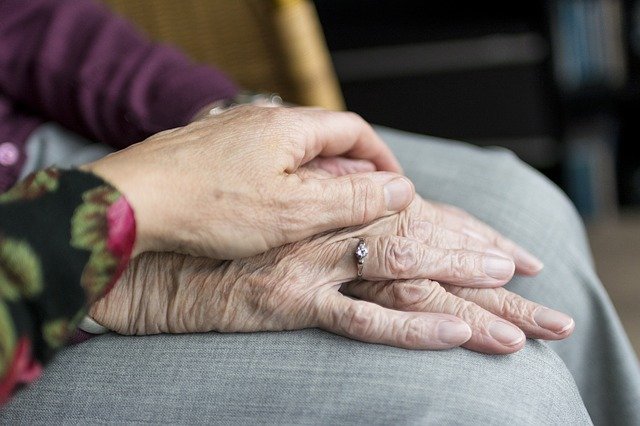 A younger person's hand over an older person's hand in care/support