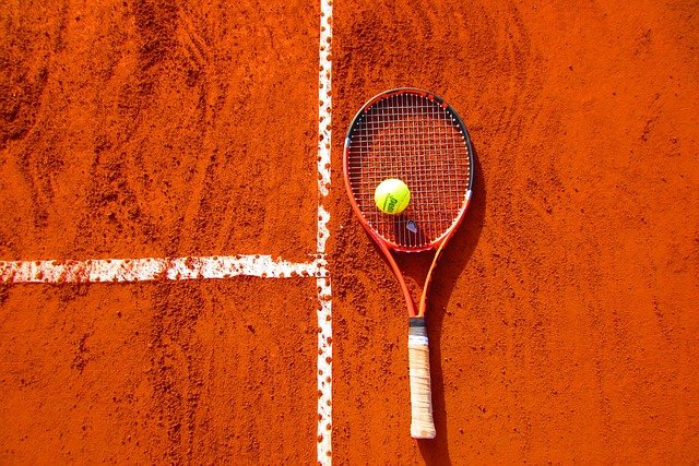 Tennis racket and ball on the floor by the lines of a clay court