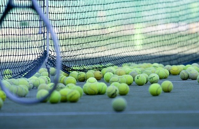 Tennis balls all gathering at the base of a tennis net with racket leaning on net