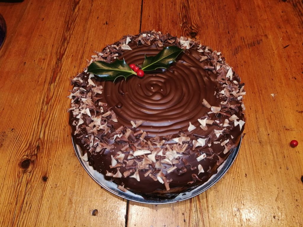 Christmas cake covered in chocolate and sprinkles and topped with holly
