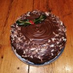 Christmas cake with chocolate icing and sprinkles topped with holly