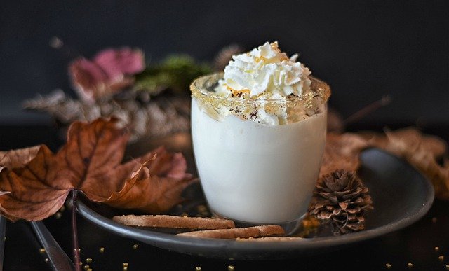 Chocolate milk with cream on top with autumn leaves scattered around the plate