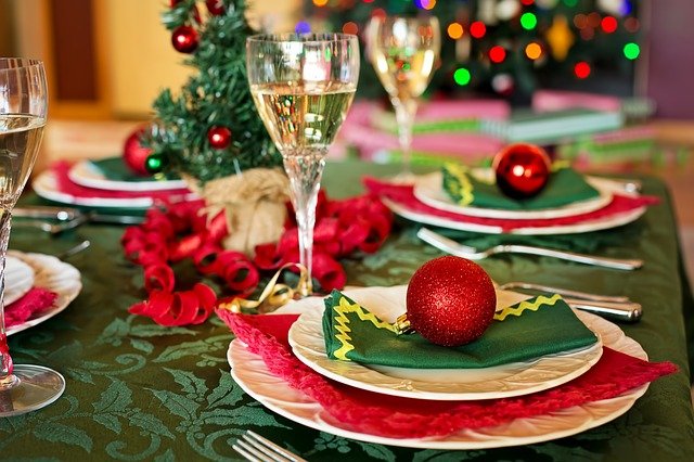 A Christmas dinner table laid with plates, napkins, baubles and glasses of wine