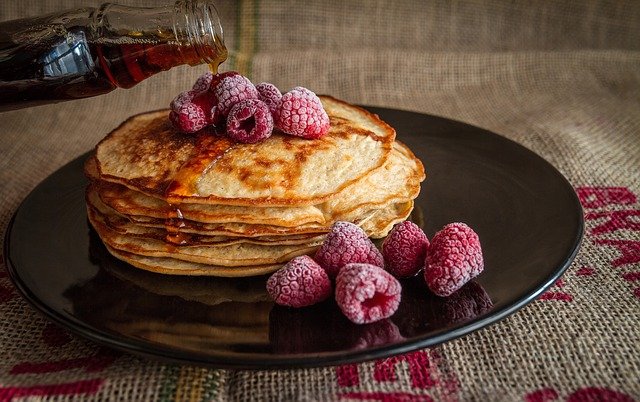 A stack of pancakes with frosted raspberries on top and by the side