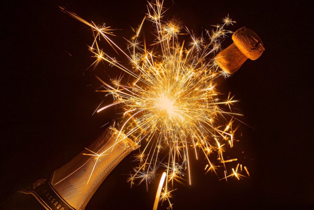 Cork popping off a bottle of champagne with sparklers fizzing out of the top